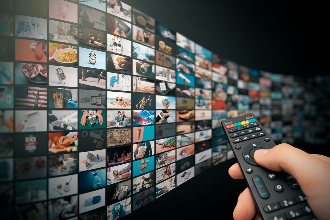 A wall of television screens with a hand holding a remote control.